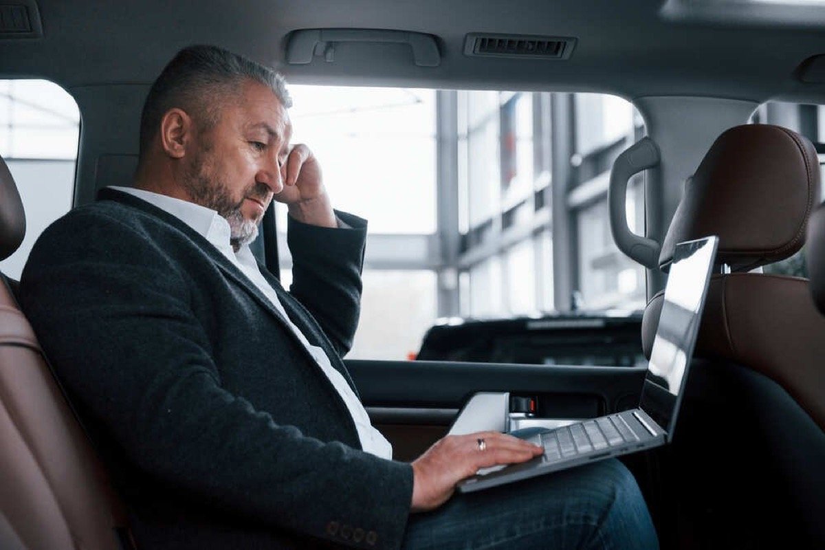 Corporate executive working productively on laptop in rear luxury SUV cabin